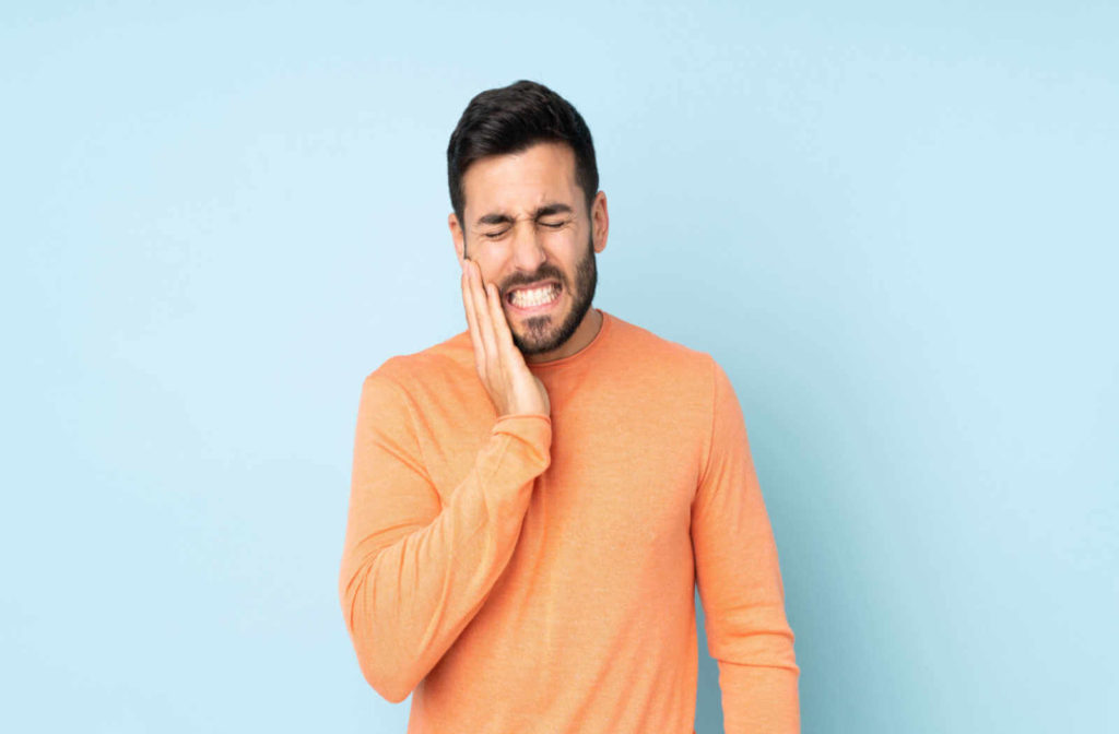a man holds his cheek while grimacing due to a toothache